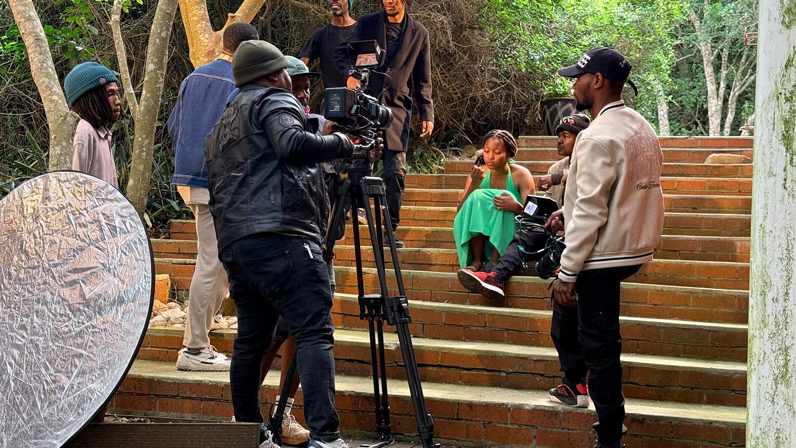 A camera crew filming on location in South Africa, cinema camera on a tripod with cast and crew on the steps